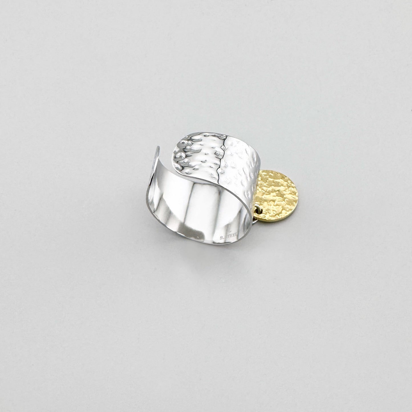 Wide stainless steel ring in silver and gold tones, adorned with a textured medallion pendant, French brand Ikita.