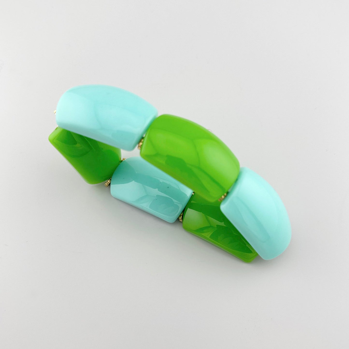 Pulsera de plástico en tonos verdes y azules con formas geométricas, marca francesa Ikita.