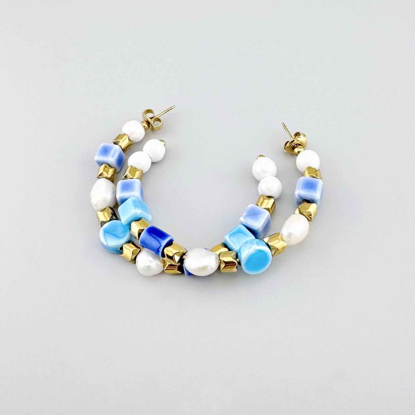 Boucles d’oreilles créoles en céramique et perles dans les tons bleus et blancs, décorées de perles dorées, marque française Ikita.