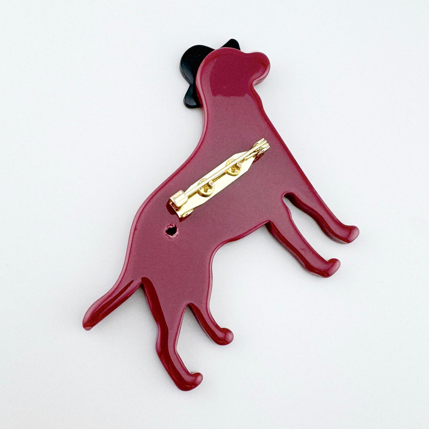 Glänzende Brosche in Form eines Hundes in Bordeauxrot mit schwarzem Hut.