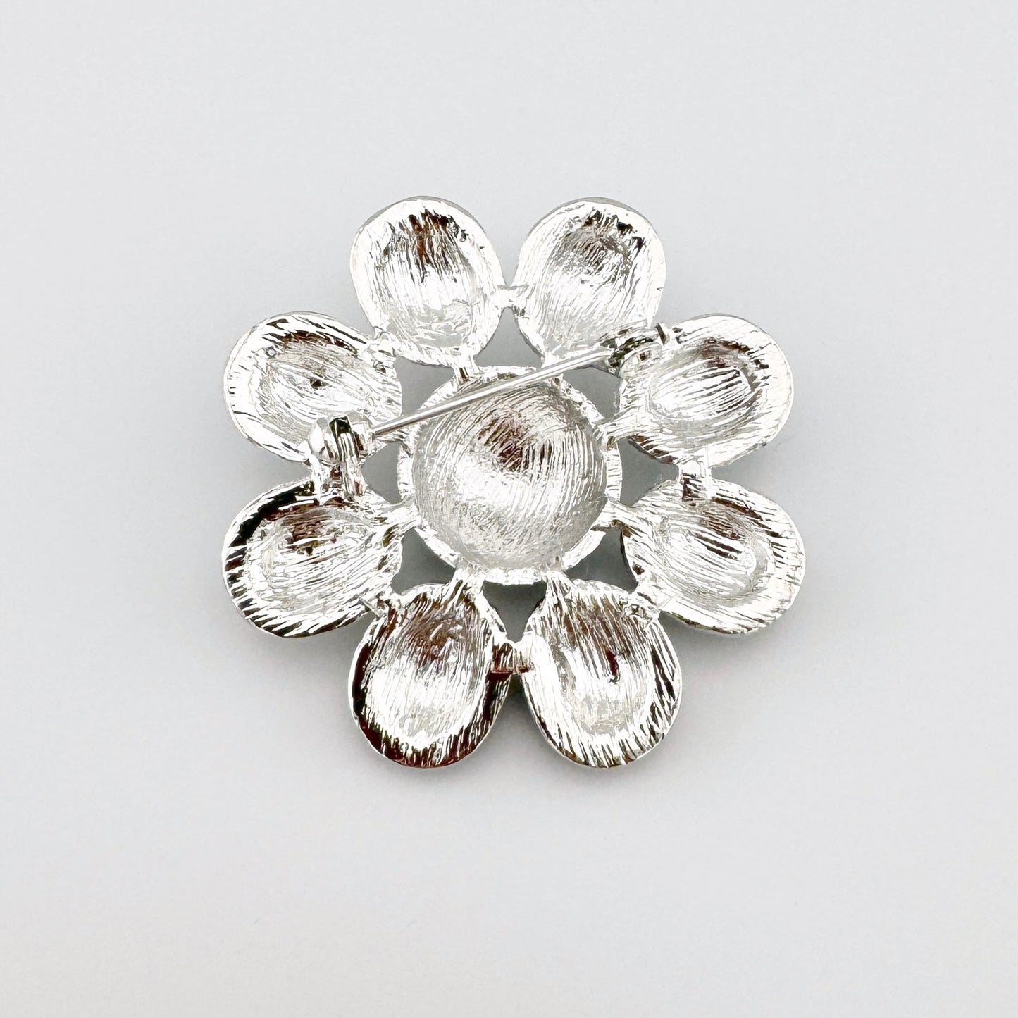 Flower-shaped brooch with gray enamel petals and a black center, decorated with shiny details.