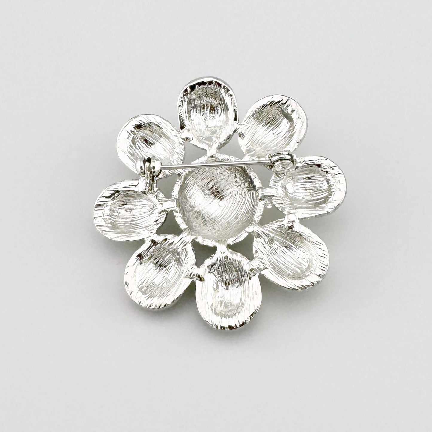 Broche en forma de flor con pétalos blancos y centro rojo, adornado con detalles brillantes.