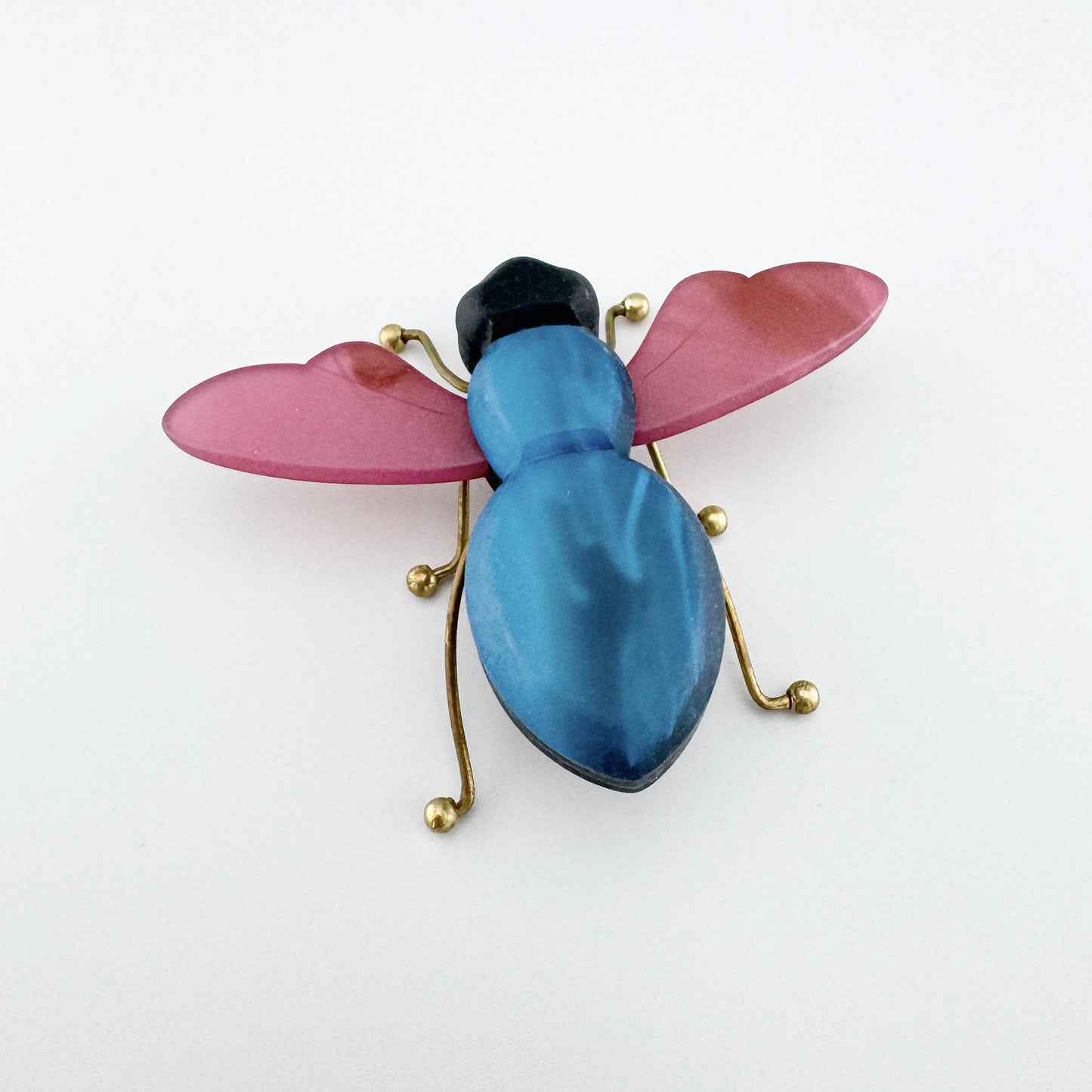 Brooch in the shape of an insect, featuring a blue body and pink wings, made of acrylic and metal.