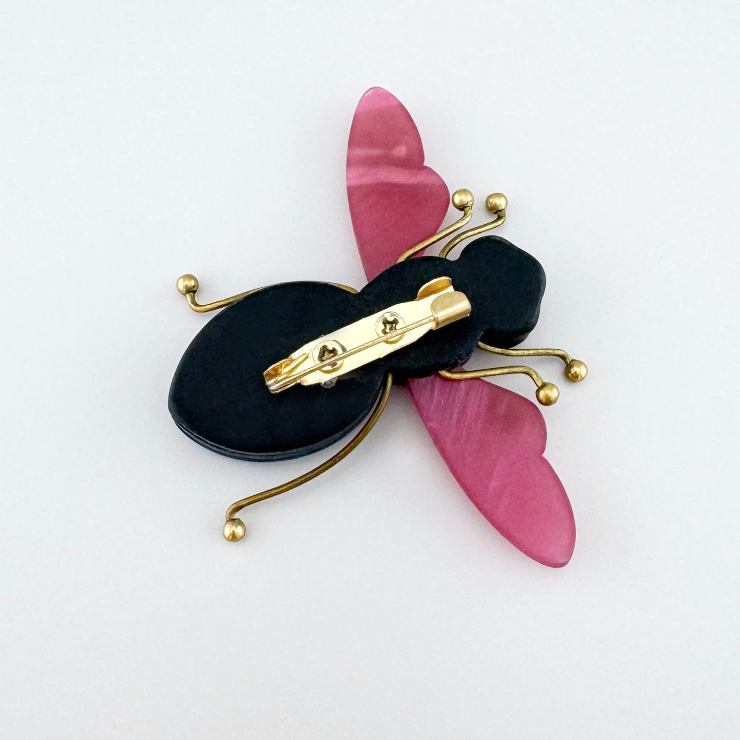Broche en forma de insecto con cuerpo azul y alas rosadas, hecho de acrílico y metal.
