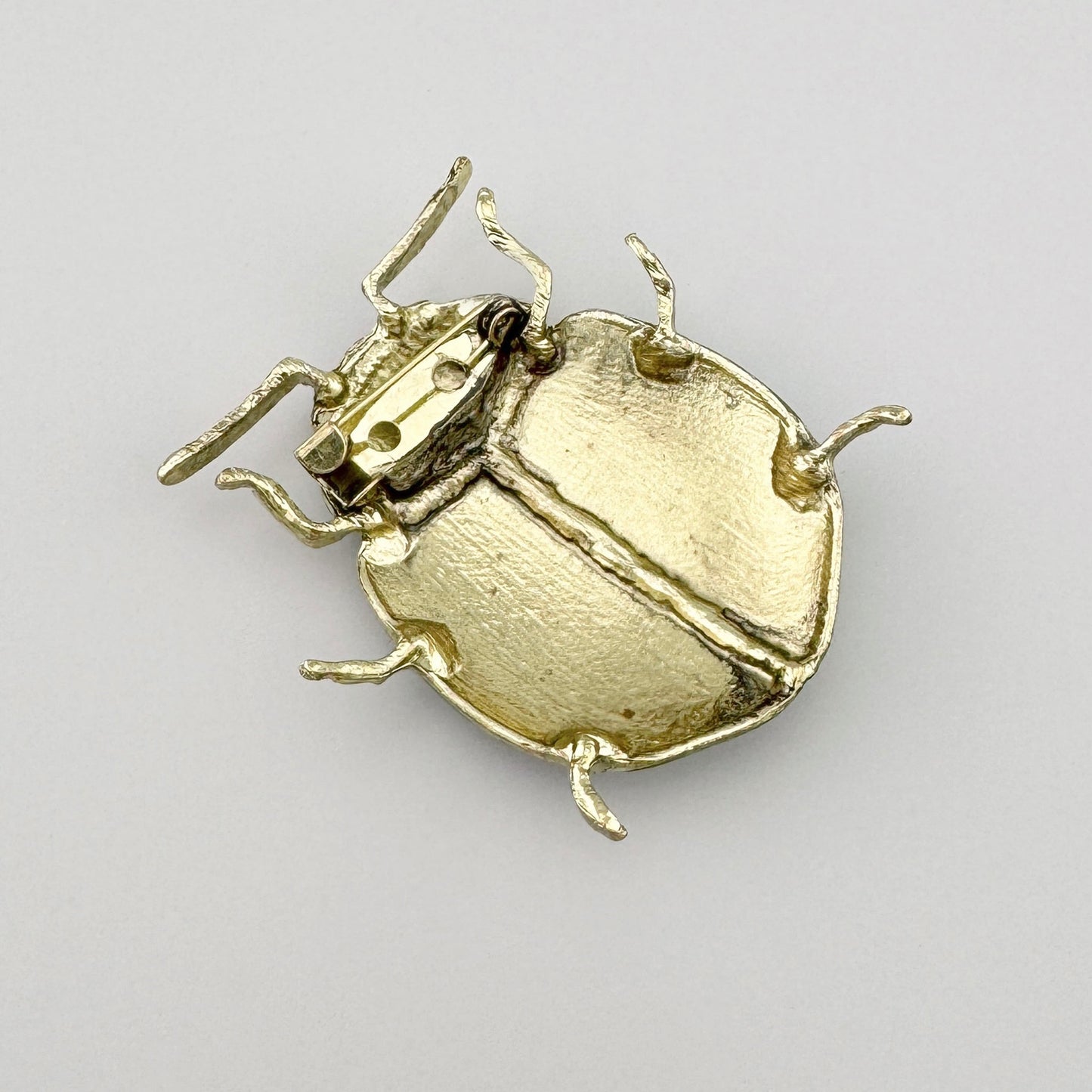 Metallene Brosche in Form eines grünen Käfers mit braunen Flecken, handbemalt.