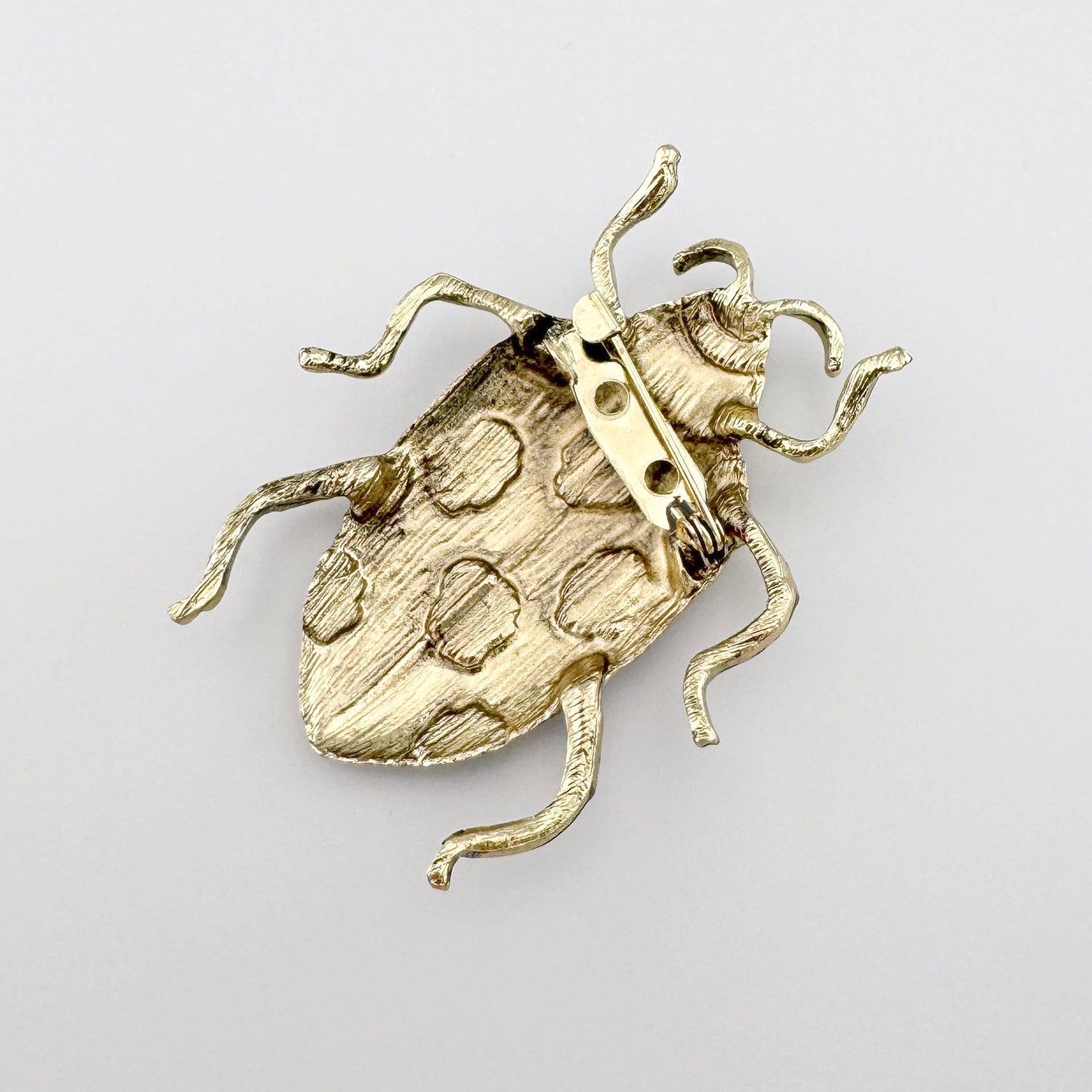 Broche en forma de escarabajo rosa, hecho de metal con manchas negras y detalles dorados.