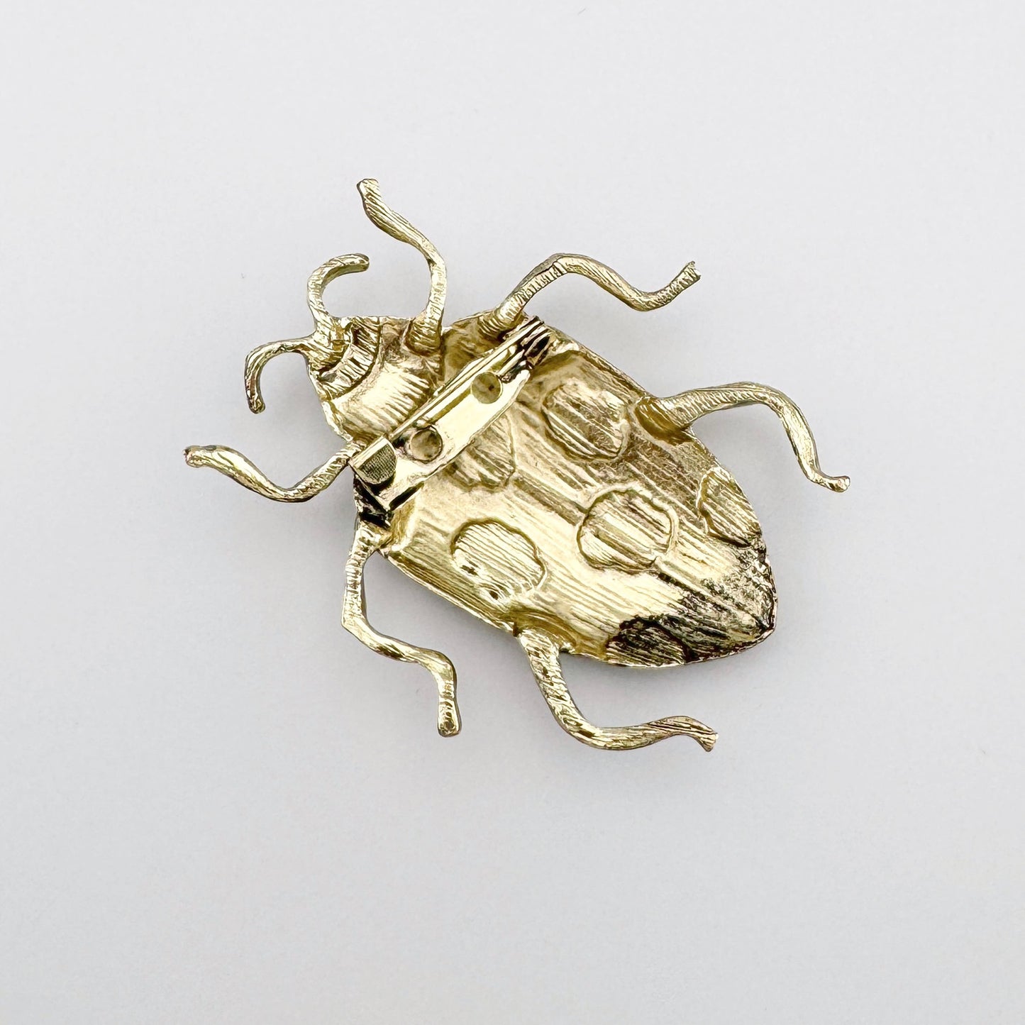 Broche en forma de escarabajo dorado con detalles negros y marrones, esmaltado.