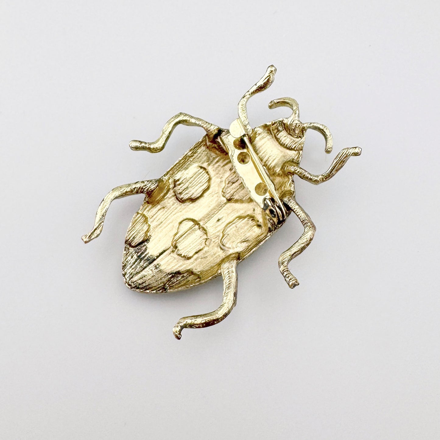 Broche con forma de insecto, de metal con esmalte verde y detalles negros.