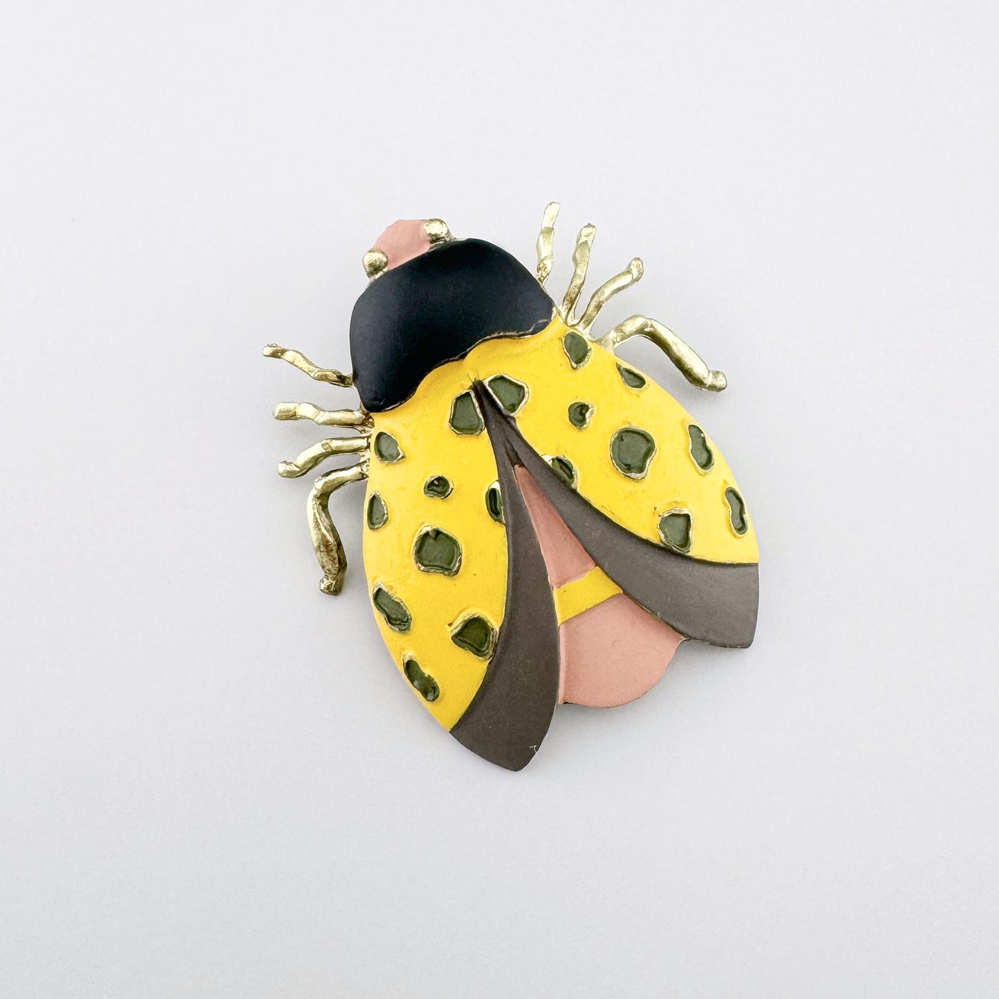 Broche en forme de scarabée dans des tons jaunes et bruns, avec des détails peints à la main.