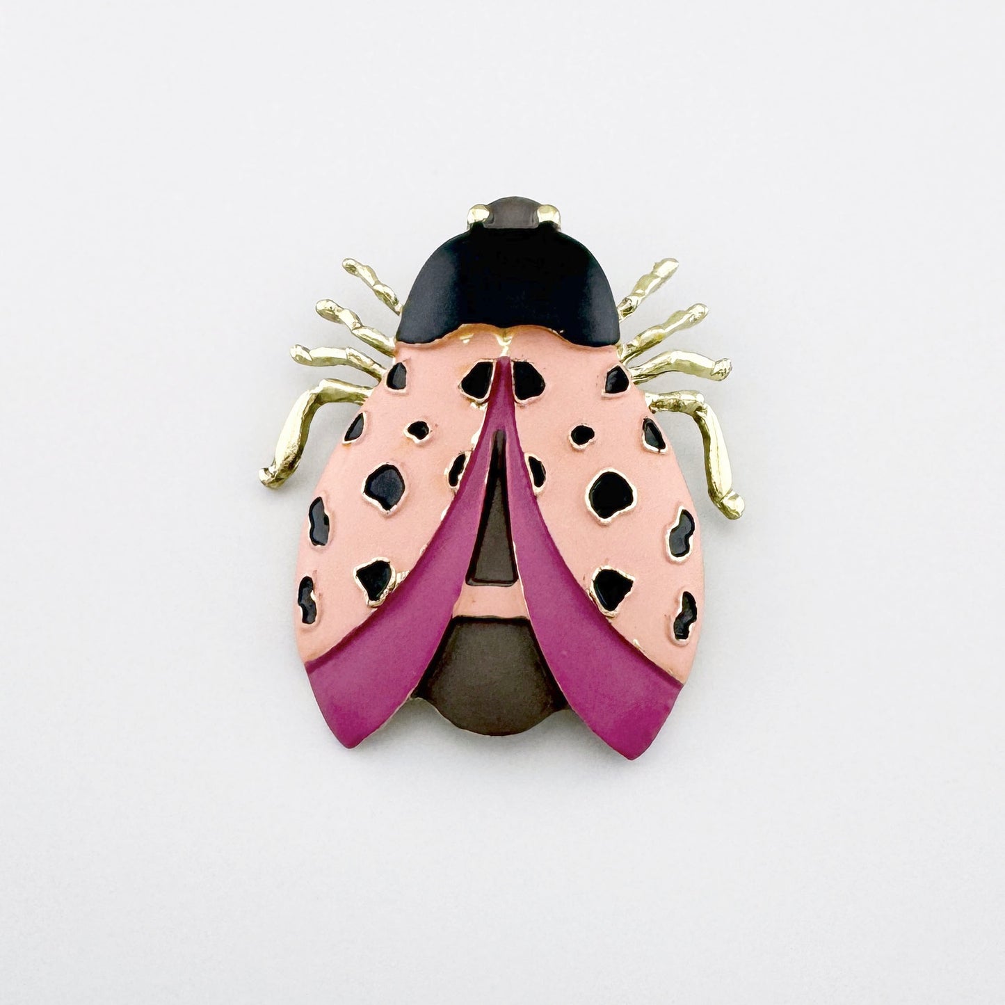 Brosche in Form eines Insekts mit Verzierungen in Rosa-, Lila- und Schwarztönen.