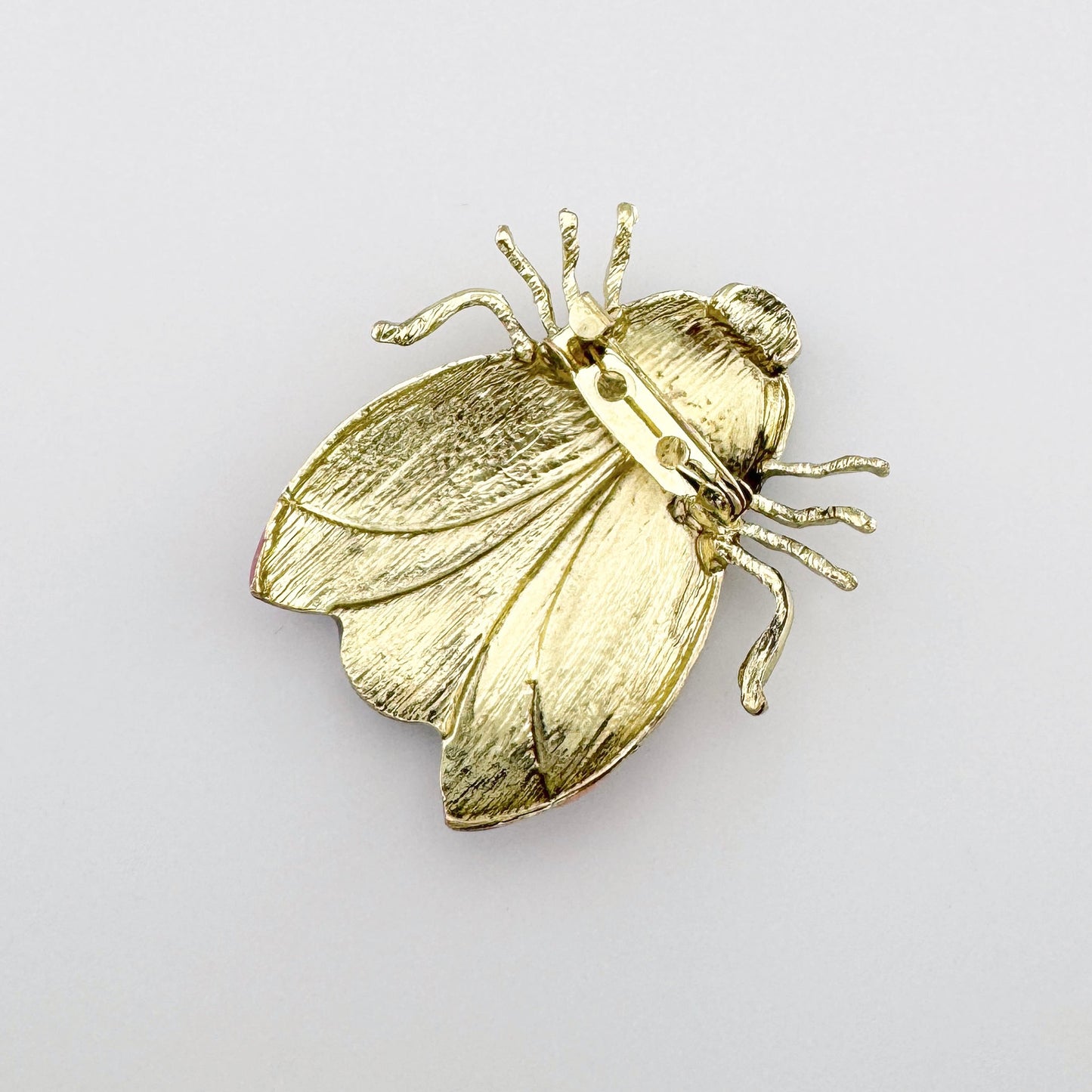 Broche con forma de insecto, decorado con detalles en tonos rosa, morado y negro.