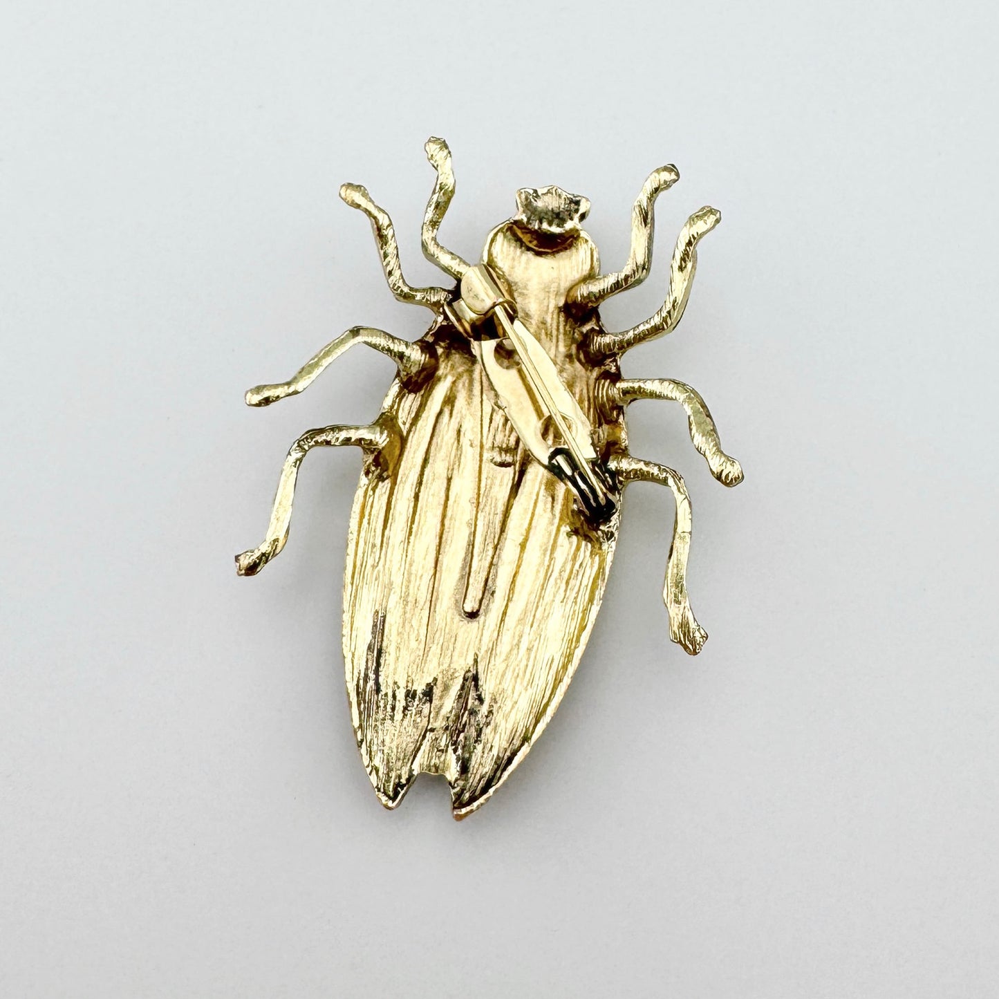 Broche en forma de escarabajo dorado con detalles negros y acabado metálico.