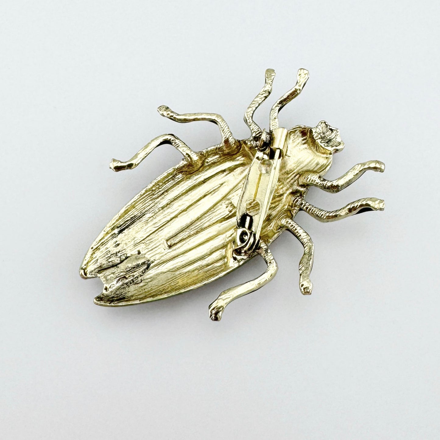 Metal brooch in the shape of a beetle, hand-painted in shades of green, pink, and black.