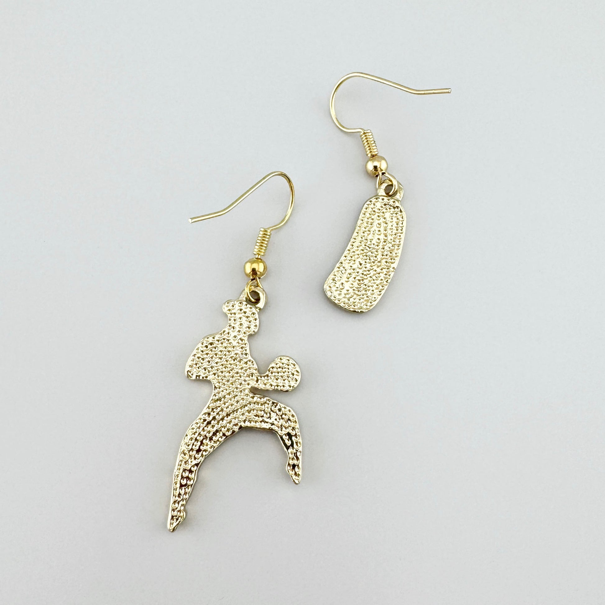 Pendientes con temática de boxeo en color dorado con esmalte rojo, que muestran a una boxeadora y un saco de boxeo.