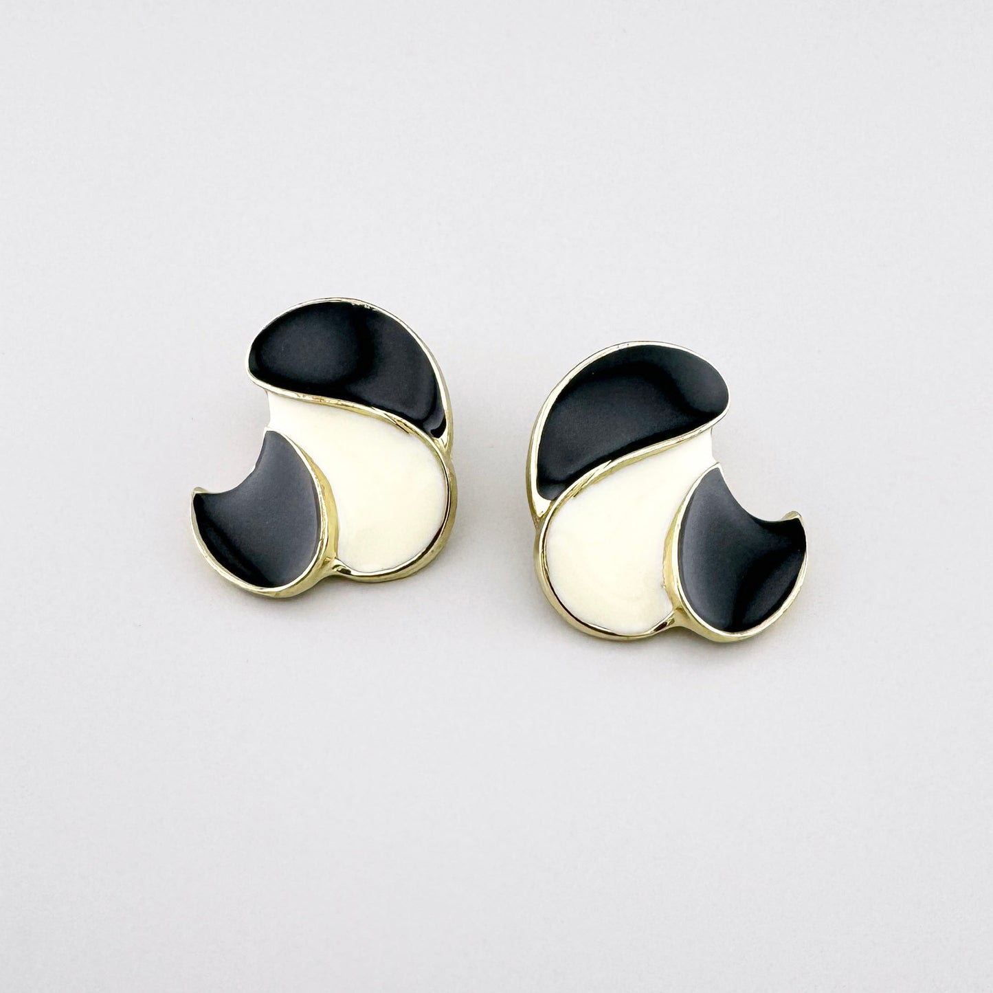 Geometrische Ohrringe mit schwarz-cremefarbener Emaille und goldener Oberfläche.