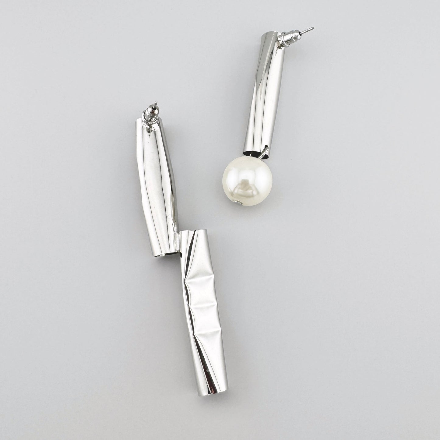 Boucles d'oreilles asymétriques argentées avec finition ondulée et perle synthétique. Marque Maravillas.