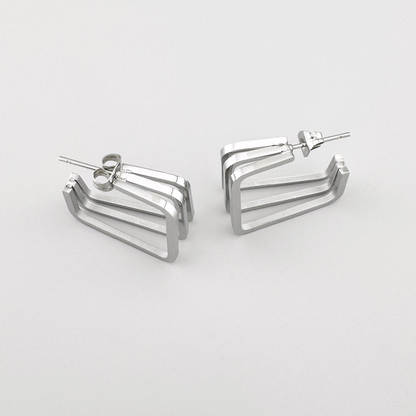Прямоугольные серьги из полированного серебристого металла с тремя параллельными линиями. Бренд Maravillas.