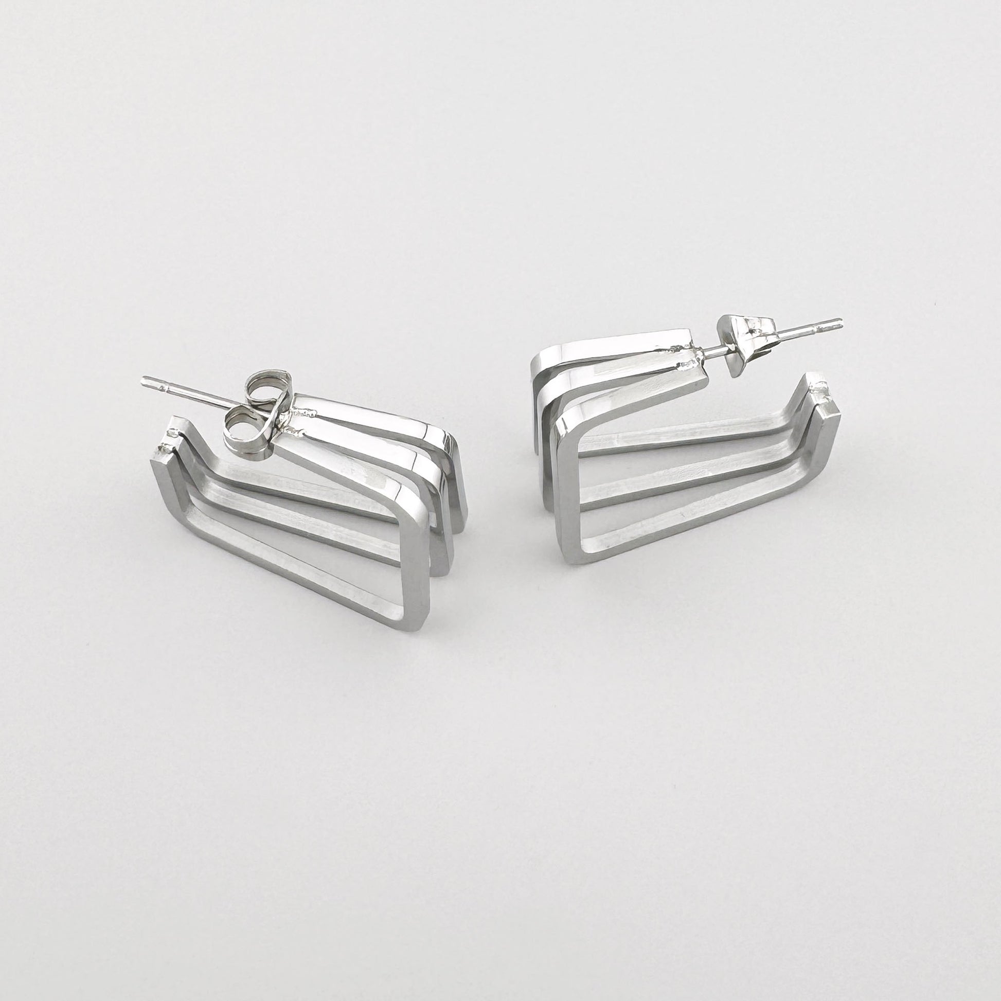 Прямоугольные серьги из полированного серебристого металла с тремя параллельными линиями. Бренд Maravillas.