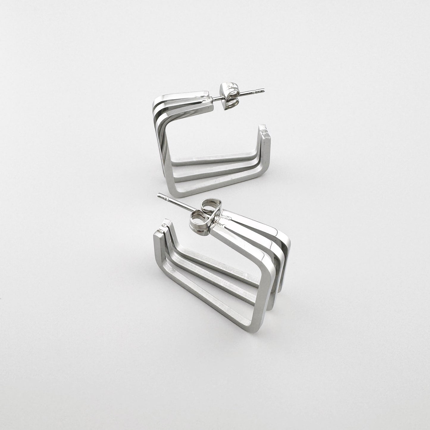Kolczyki prostokątne z polerowanego srebrnego metalu z trzema równoległymi liniami. Marka Maravillas.