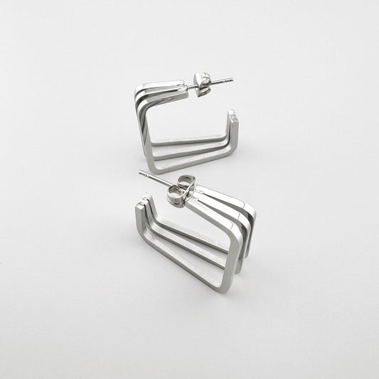 Kolczyki prostokątne z polerowanego srebrnego metalu z trzema równoległymi liniami. Marka Maravillas.