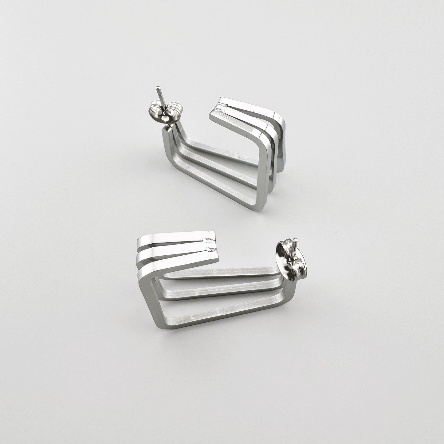 Rechteckige Ohrringe aus poliertem Silbermetall mit drei parallelen Linien. Marke Maravillas.