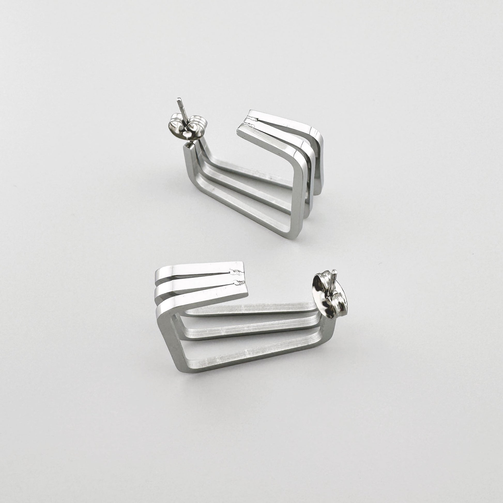 Rechteckige Ohrringe aus poliertem Silbermetall mit drei parallelen Linien. Marke Maravillas.