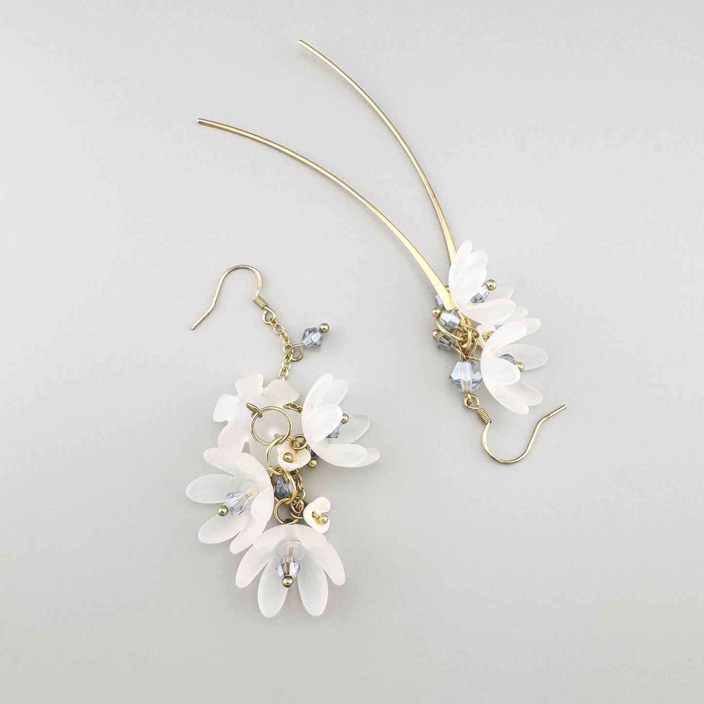 Asymmetrical earrings in a gold tone with white floral details and crystals, by Spanish brand Sonata.