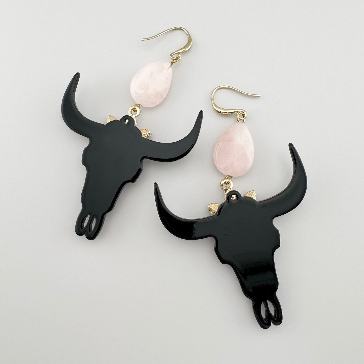 Boucles d'oreilles avec crâne de taureau noir, ornées de cristaux roses en forme de fleur et d'un quartz rose.