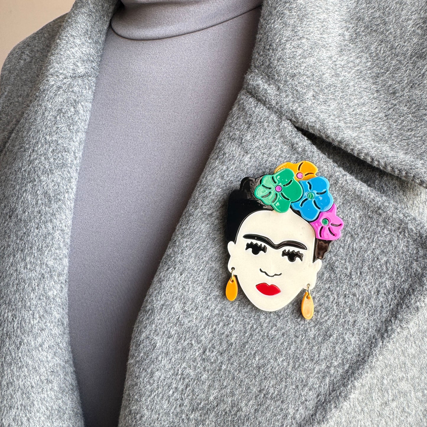 Frida Kahlo face-shaped brooch with colorful flowers and orange earrings, Spanish brand Sonata.
