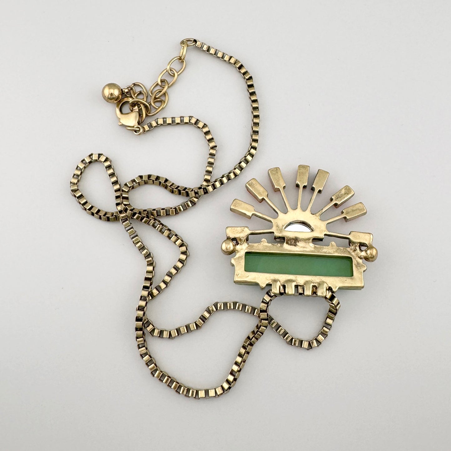 Collier artistique avec pendentif vert et orange sur chaîne dorée.
