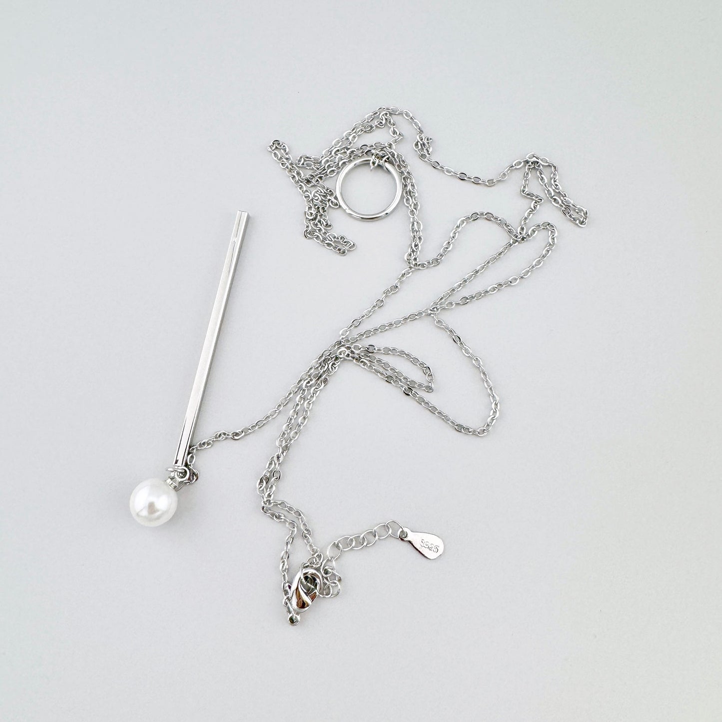 Collier de couleur argentée avec une perle délicate et un long élément suspendu, marque espagnole Maravillas.