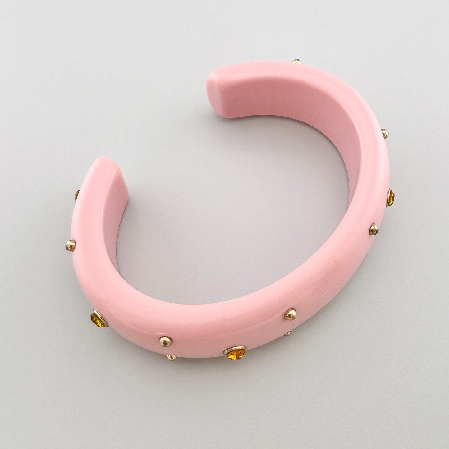 Pink bracelet made of plastic, decorated with golden studs and crystals.