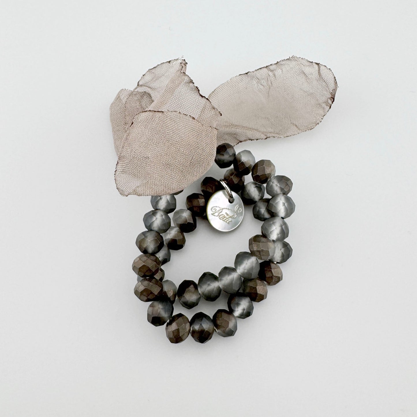 Pulsera con cuentas facetadas en tonos marrón y gris, adornada con una flor de tela beige.