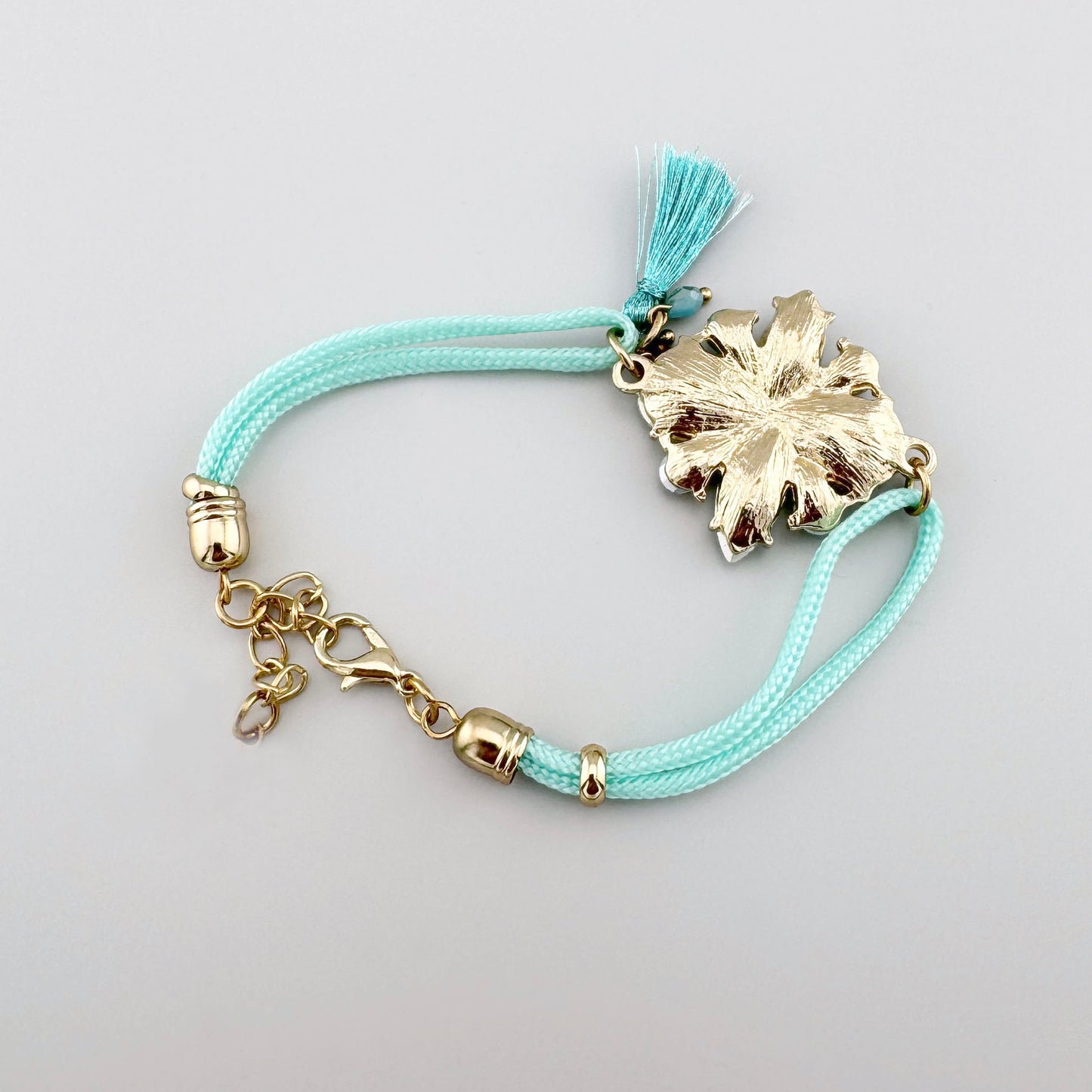 Bracelet avec sangle tressée turquoise et cristaux en forme de fleur.