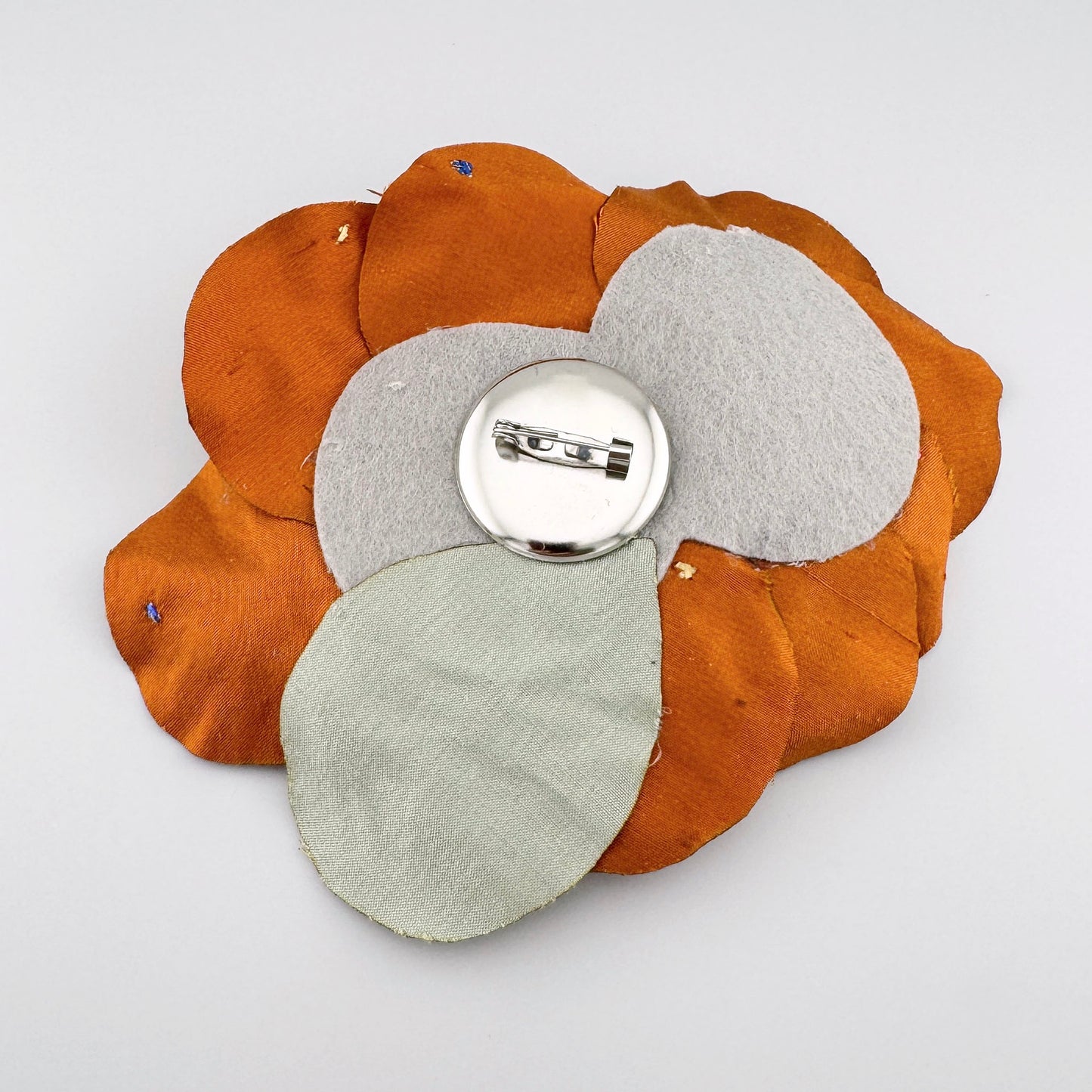 Blumenförmige Brosche aus orangefarbener Seide, verziert mit bunten Perlen und Kristallen.