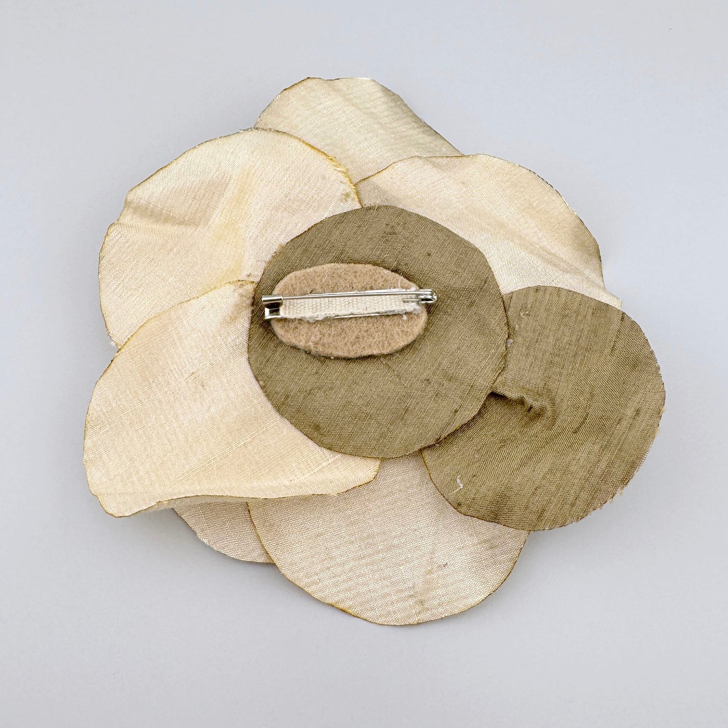 Кремовая брошка в форме цветка из шелка, украшенная жемчугом, кристаллами и разноцветными бусинами.