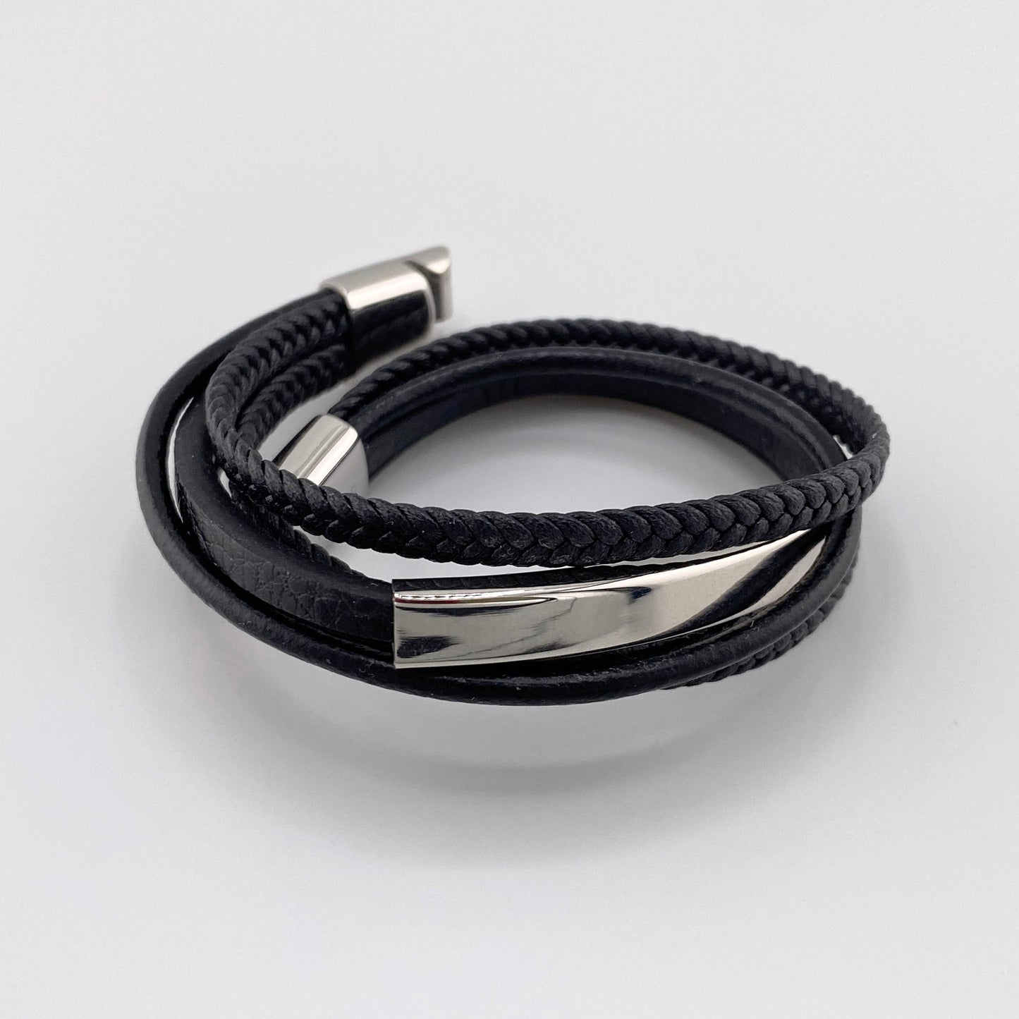 Pulsera para hombre de cuero negro genuino con tiras trenzadas y lisas, decorada con un elemento de acero inoxidable en color plateado y cierre magnético, marca francesa IRL.