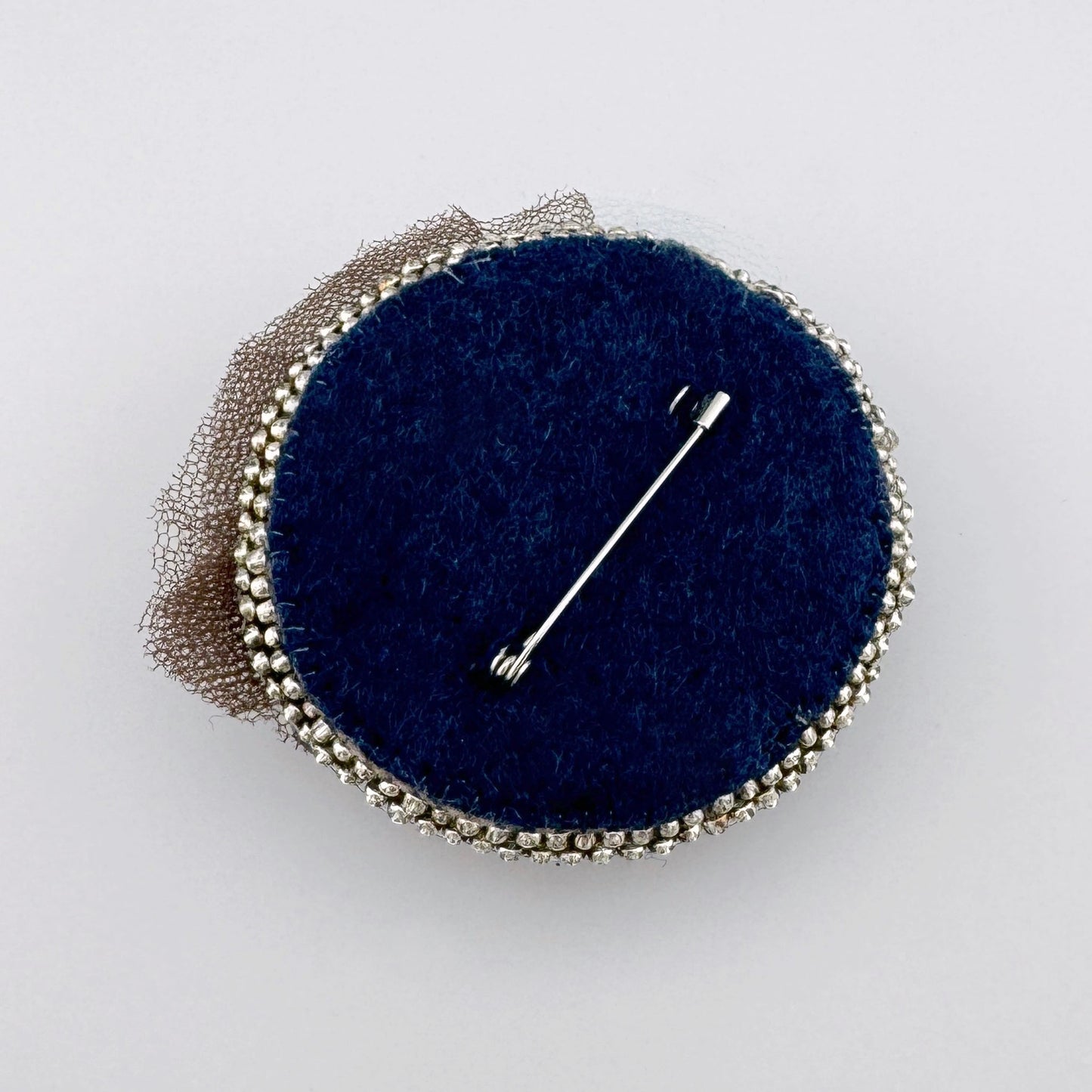 Broche redondo hecho a mano con cuentas en tonos azul marino, verde y plateado, con una capa de malla delicada.