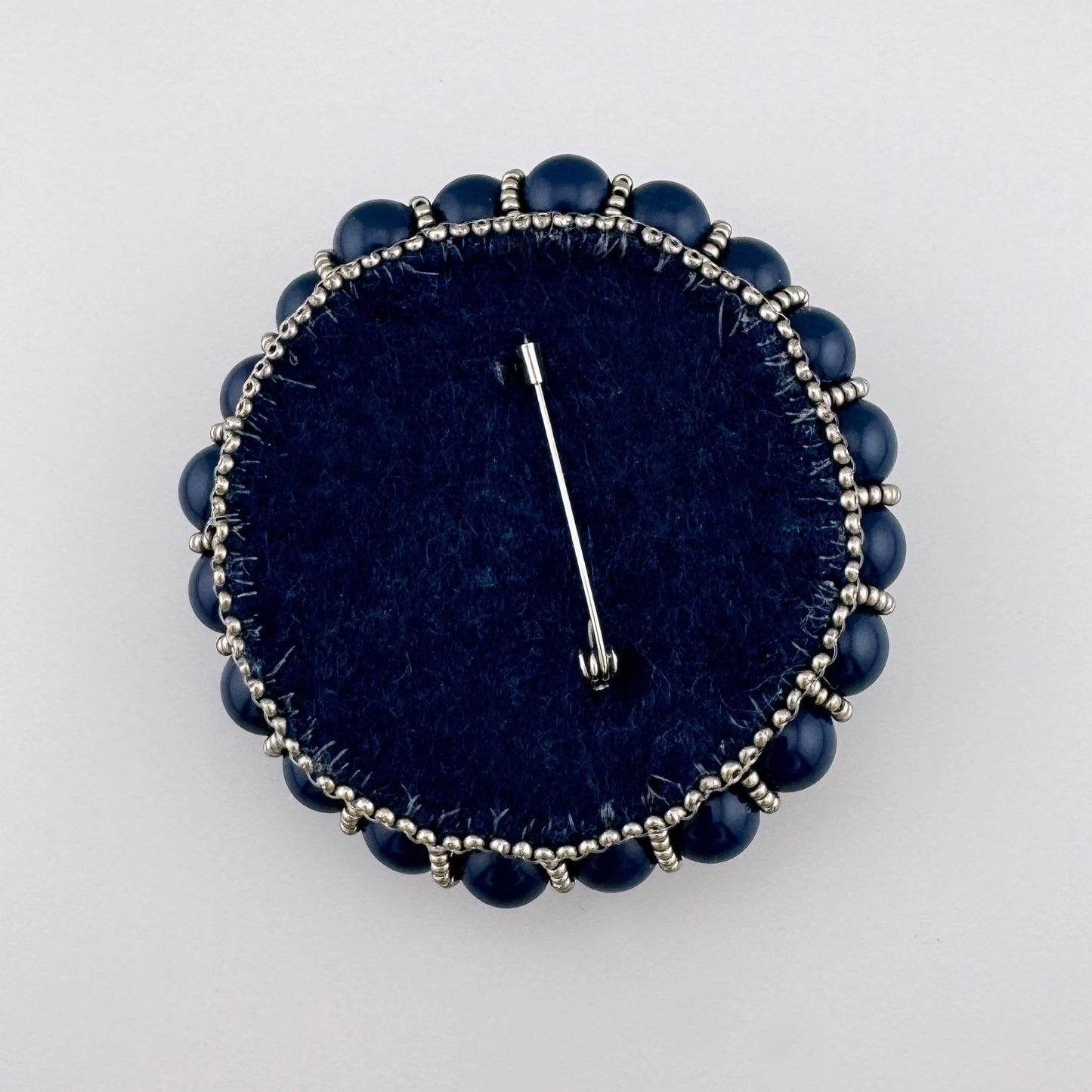 Broche hecho a mano con cuentas azul marino, verdes y plateadas dispuestas en un patrón en capas.