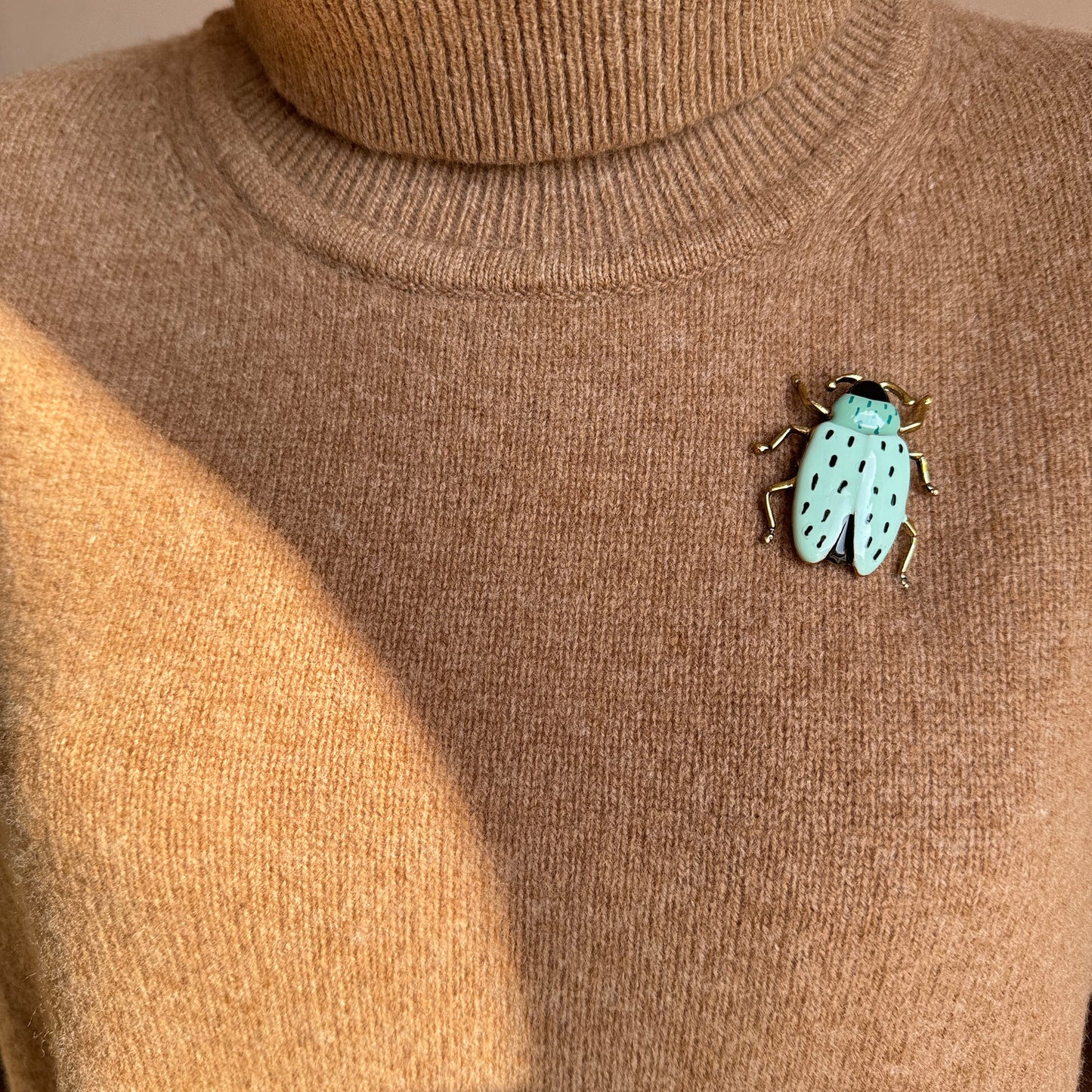 Retro beetle-shaped brooch with turquoise enamel and gold details worn on sweater