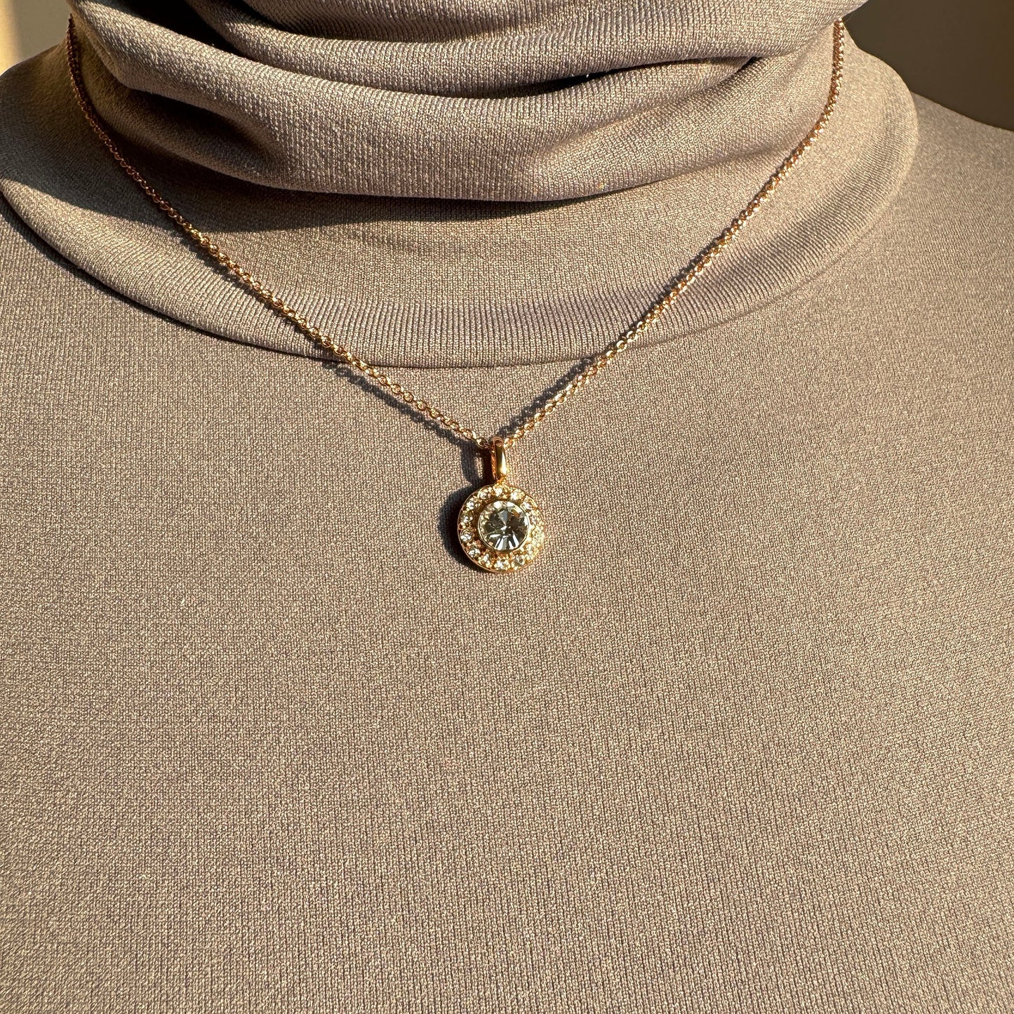 Elegant gold-plated necklace with round zirconia pendant styled on a beige top