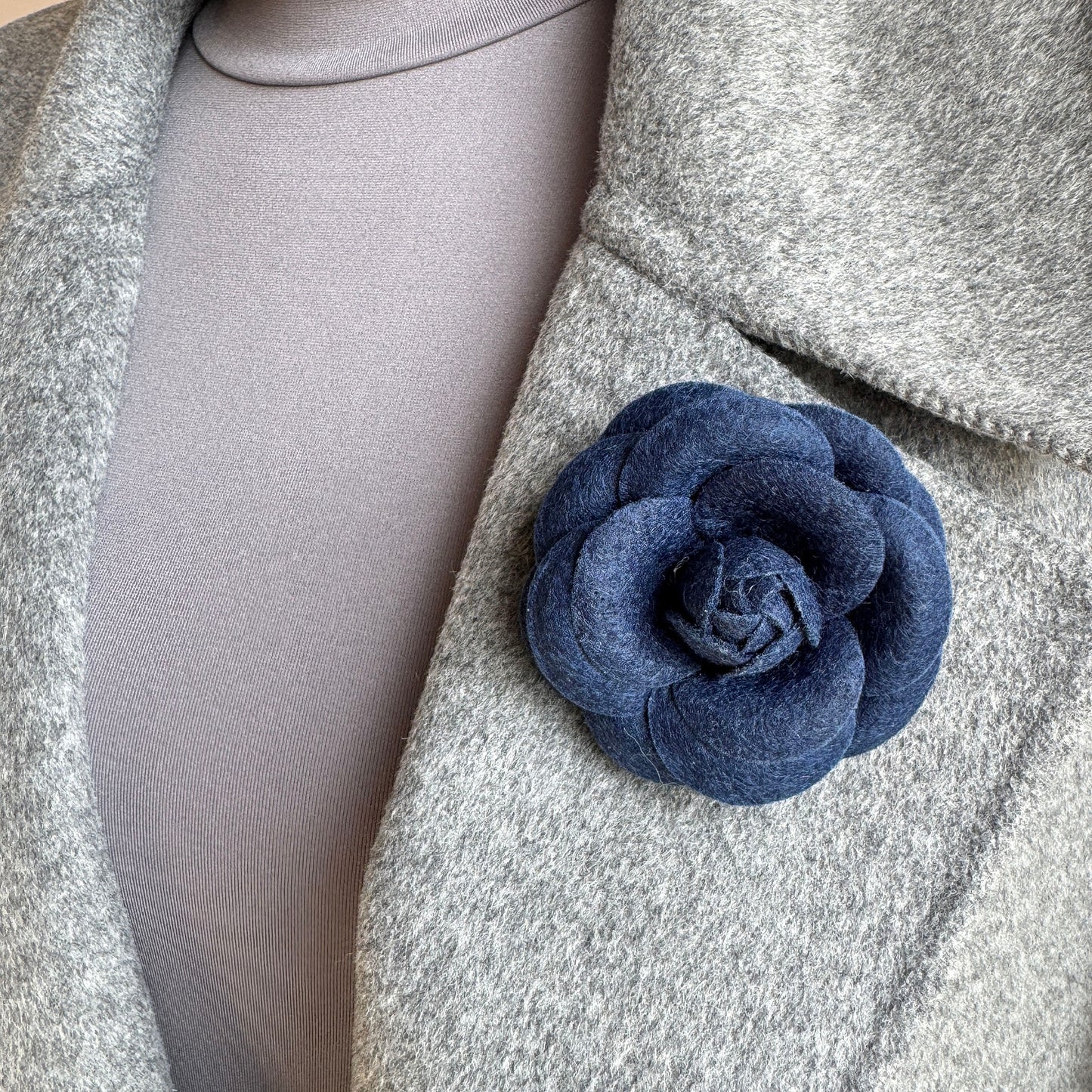 Elegant felt flower brooch in navy blue worn on a gray coat