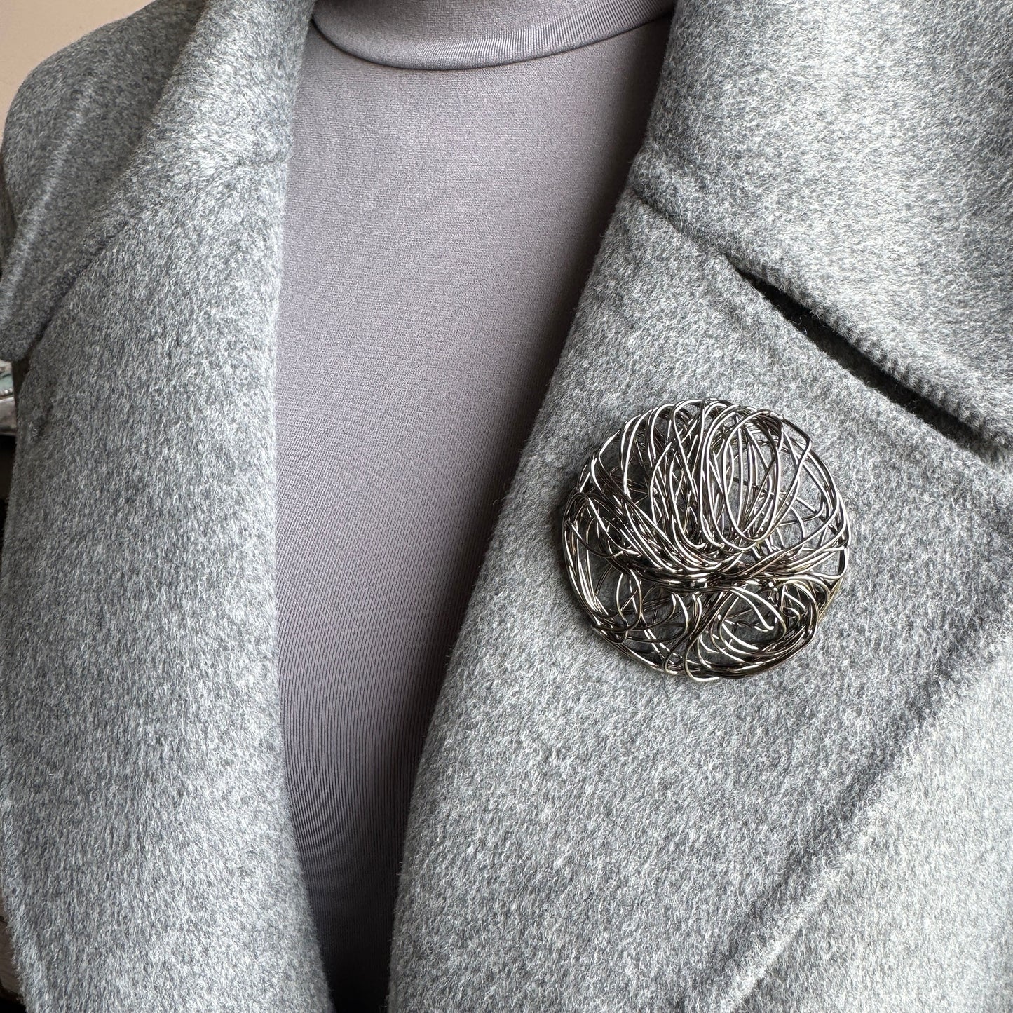 Large round geometric brooch in metal mesh design worn on coat