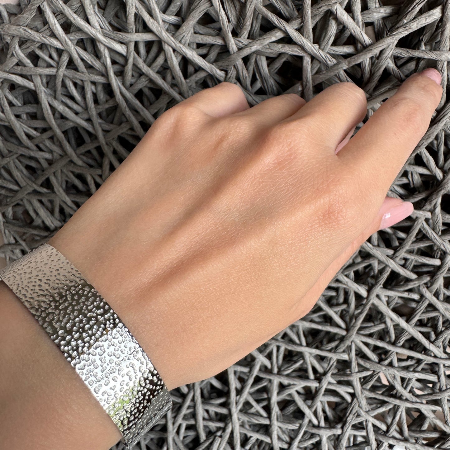 Hammered silver cuff bracelet worn on wrist, industrial minimalist style