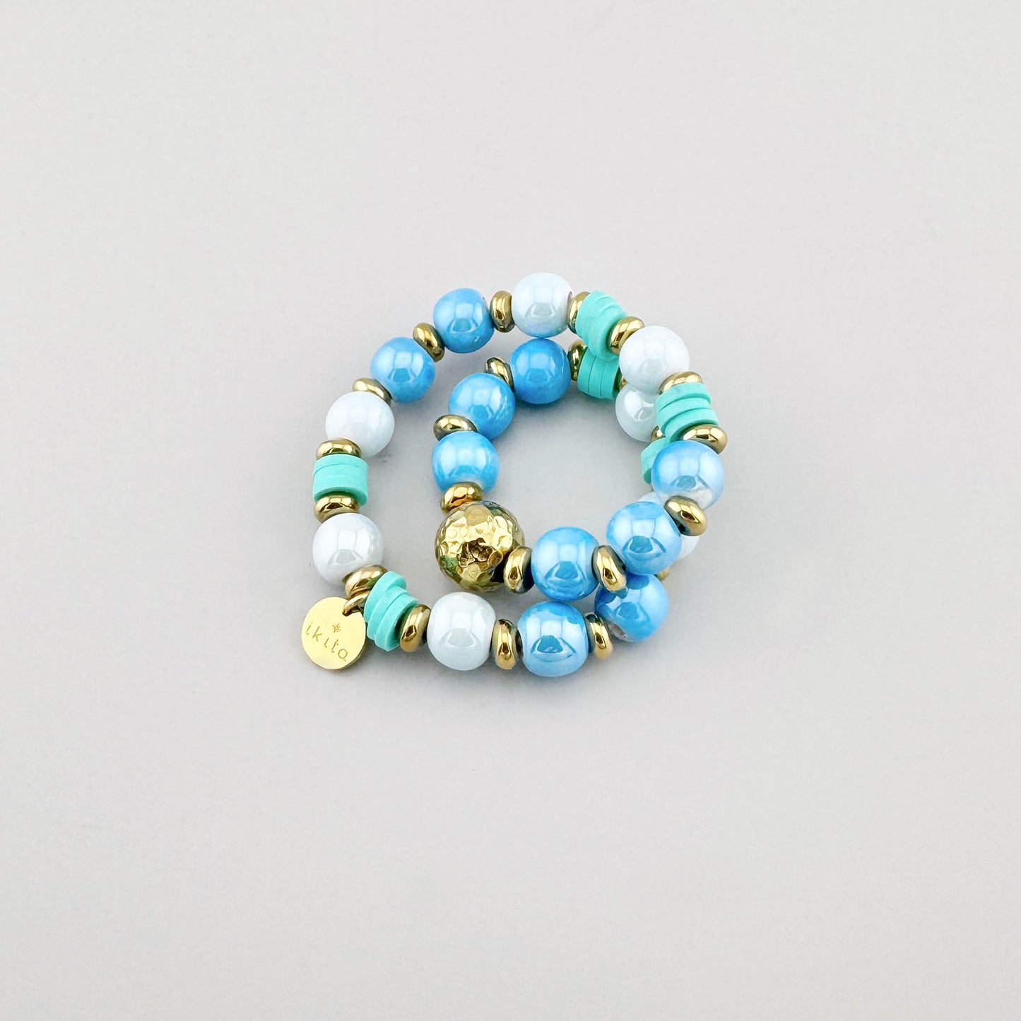 Armband aus blauen und weißen Perlen mit türkisfarbenen und goldenen Elementen, Marke Ikita.