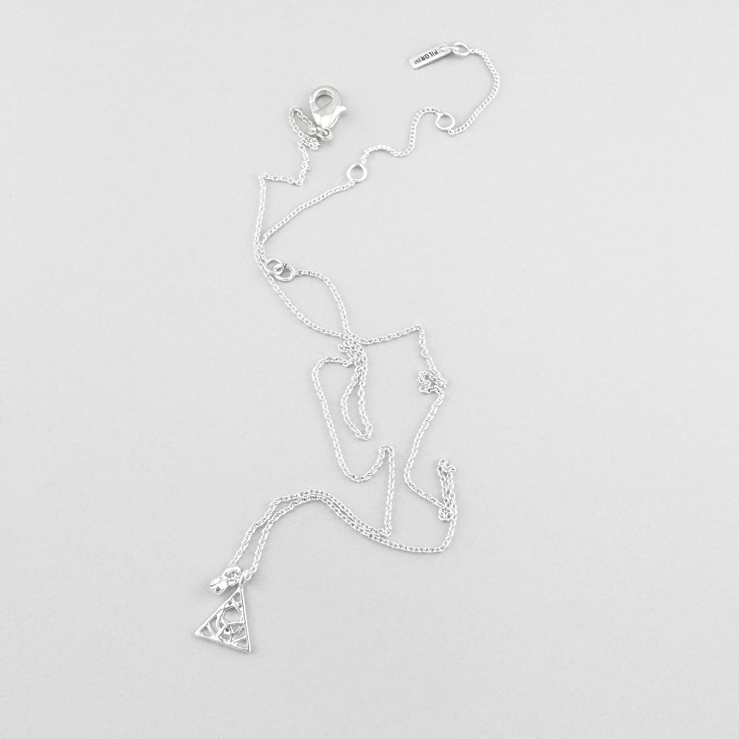 Pilgrim necklace with triangle charm and crystal arranged on light background
