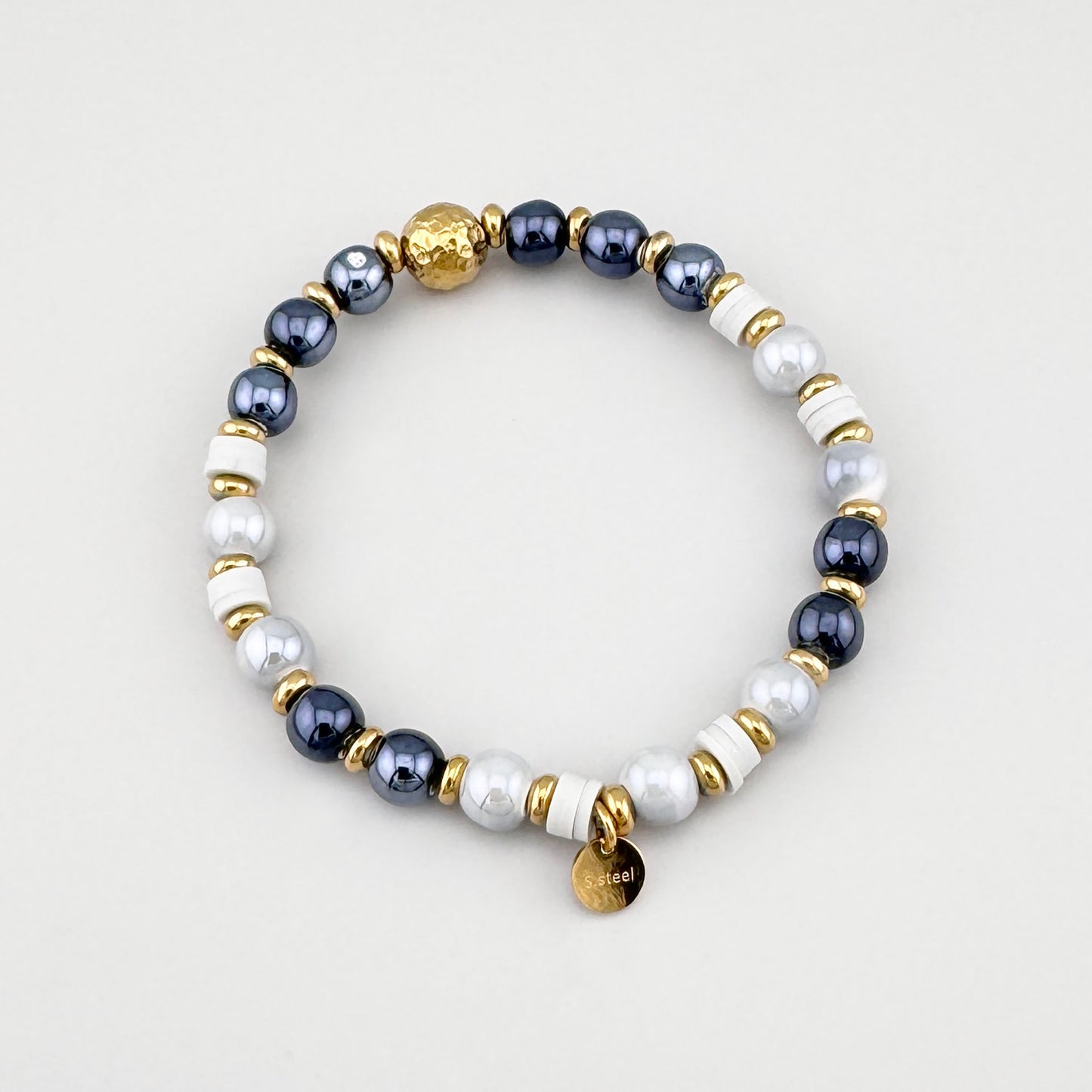 Pulsera con cuentas grises y blancas con detalles dorados dispuesta en círculo