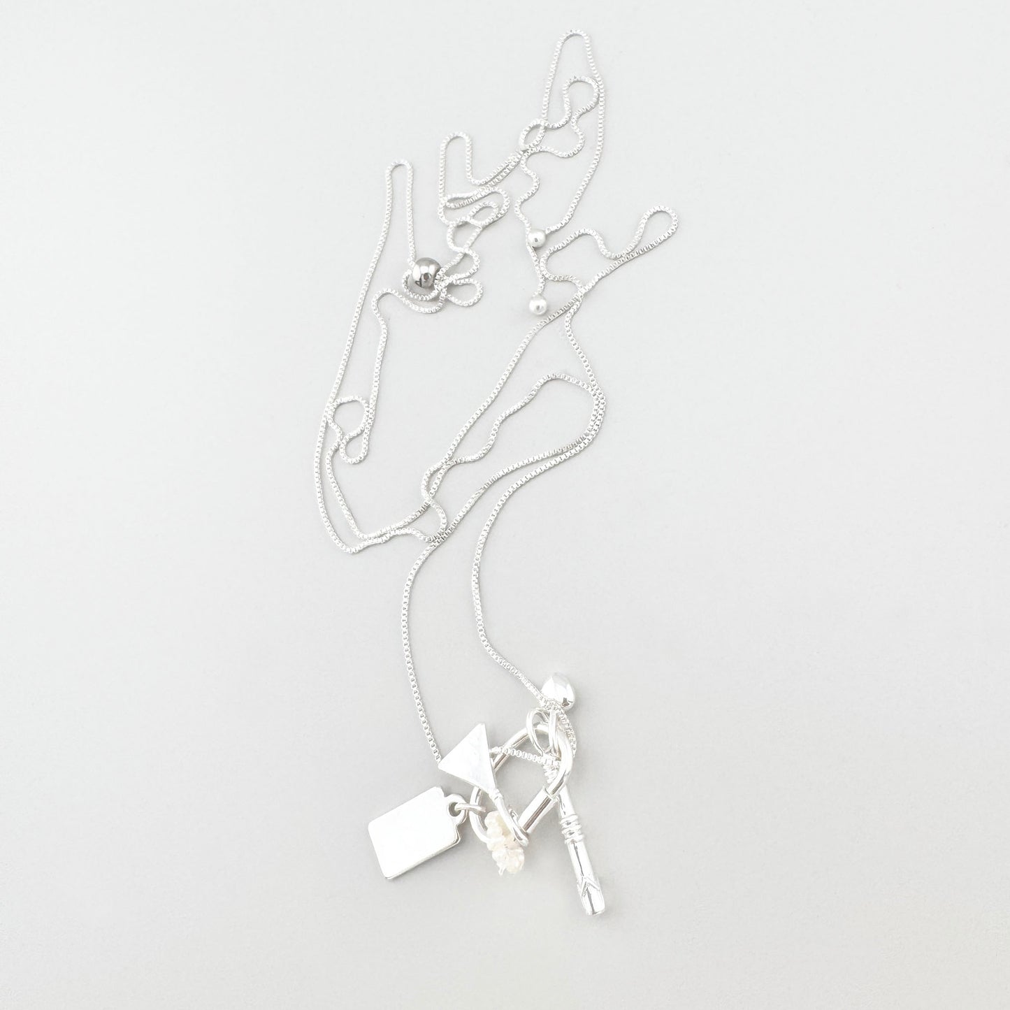 Collier argenté Pilgrim avec breloques disposé sur fond clair