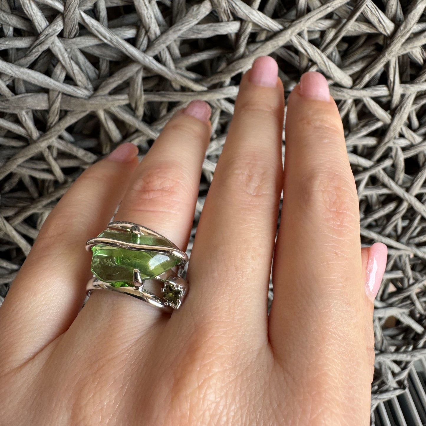 Bold silver ring with green crystal worn on hand in sunlight