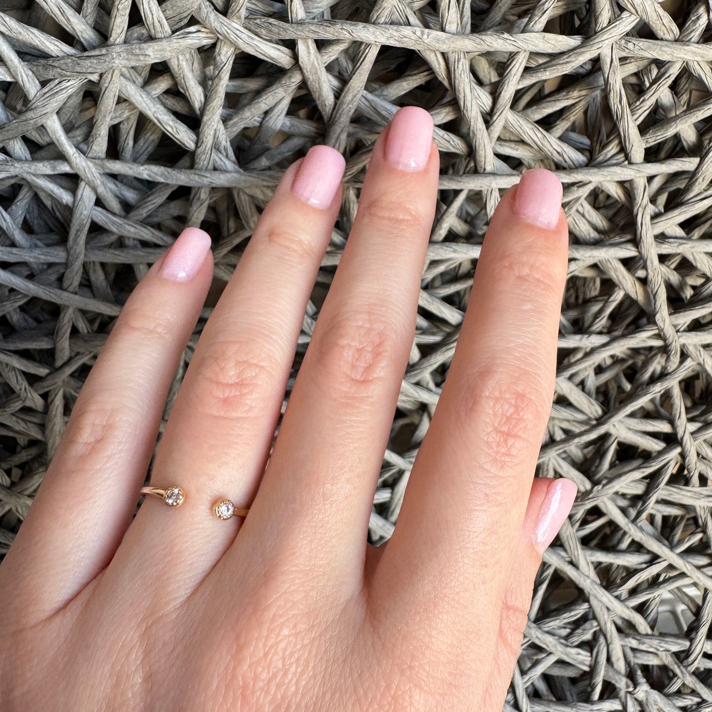Small gold IRL open ring with two cubic zirconias worn elegantly on hand